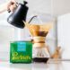 A hand holding a water container pouring into a pour-over with a green Partners Coffee box in front of it