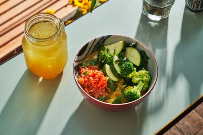 A bowl of vegetables with an orange drink beside it on a teal placemate