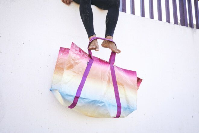 A person hanging their feet down. Around their feet is a rainbow striped tote bag