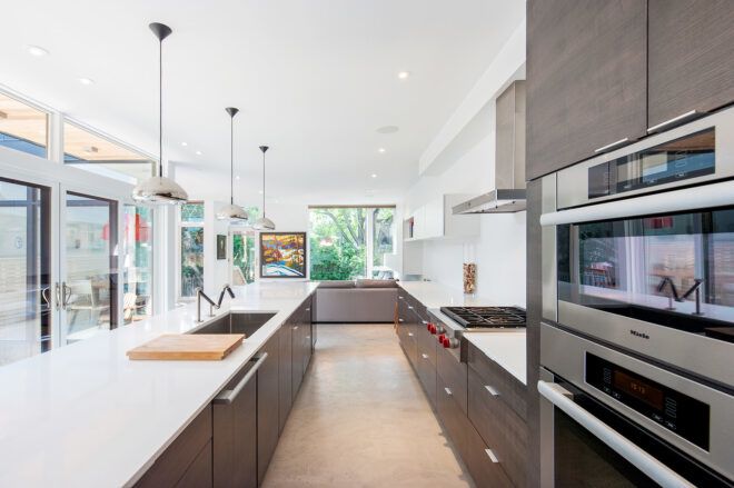 An interior kitchen has ovens on a wall beside the stove and across from the stove is the sink