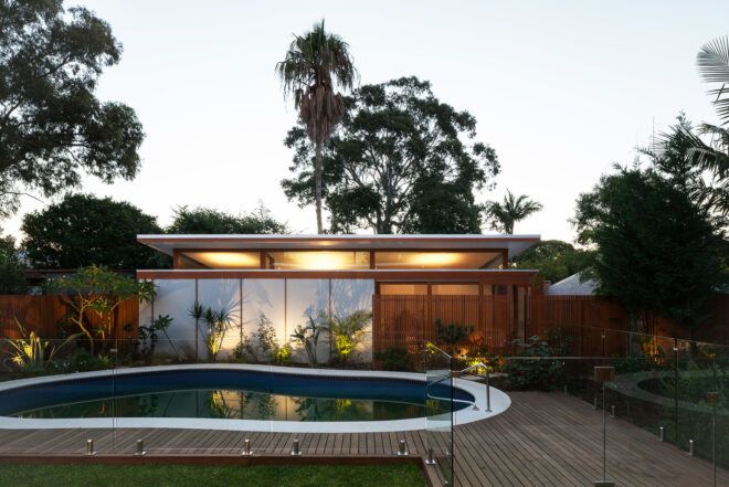 A one-story house with lights on its overhang sits in front of a pool with its green design
