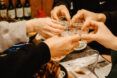 Five hands holding a glass shot up filled with soju