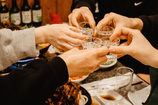 Five hands holding a glass shot up filled with soju