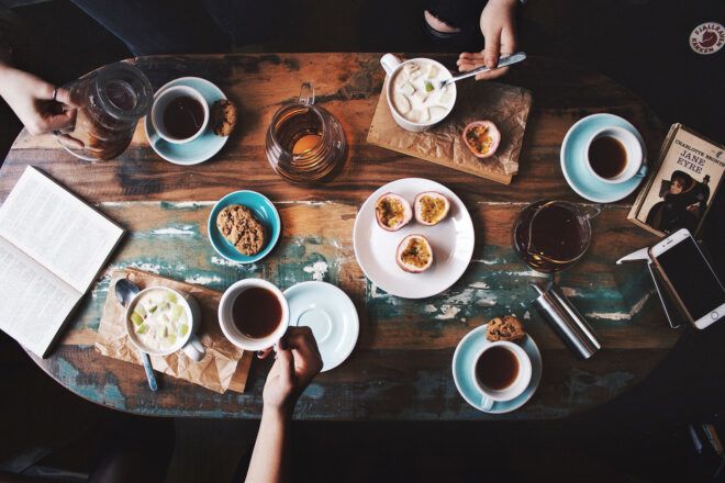 A table spread filled with cups of coffee, plate of pastries and utensils