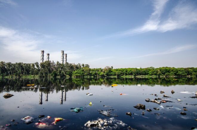 A stream polluted with different plastic waste beside a factory in the distant background