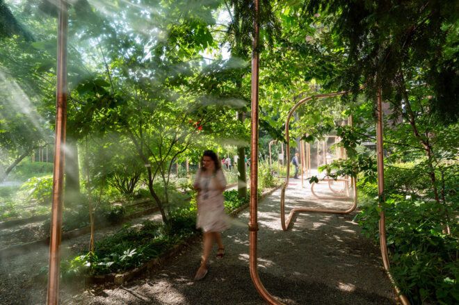 A pathway with copper piping and a girl walking through it