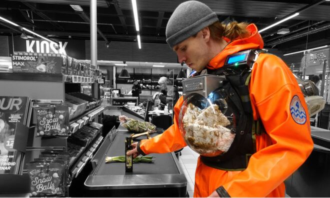 A man wearing an orange suit with a contraption strapped to his chest that contains mealworms inside eating plastic
