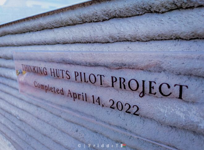 Text on the side of a building reading "Thinking Huts Pilot Project" and underneath "Completed April 14, 2022"