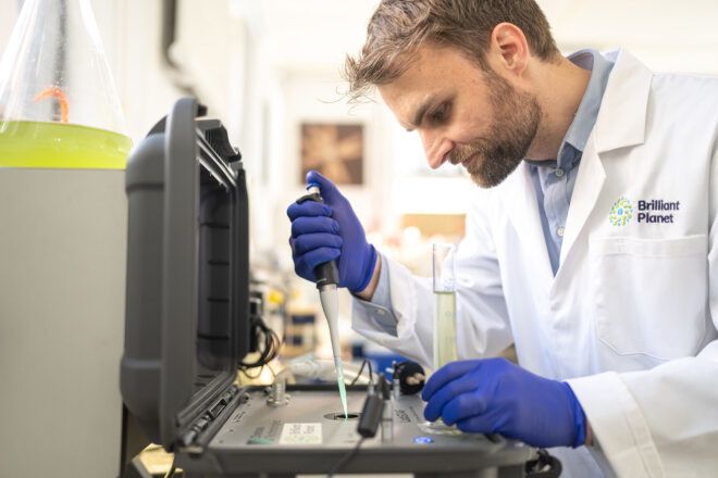 A man in a research lab coat and blue gloves experiments