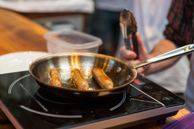 Sausages cooking in a steel pan on an electric stove