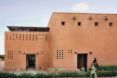 Woman walking in front of a earthy red brick building that has rectangular perforations