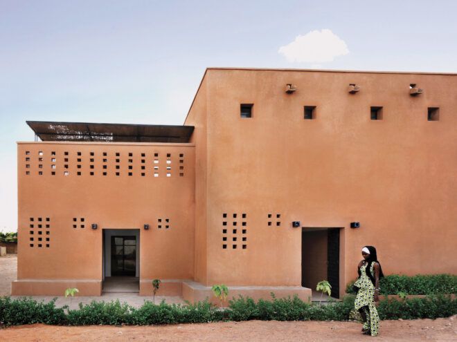 Woman walking in front of a earthy red brick building that has rectangular perforations