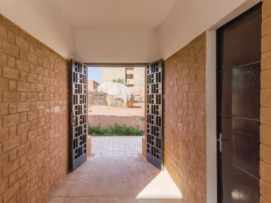 View out from entry passageway with two doors that have rectangular perforations that mimic the brick masonry of the building walls