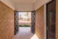 View out from entry passageway with two doors that have rectangular perforations that mimic the brick masonry of the building walls