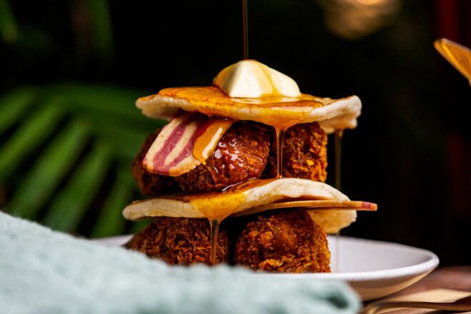 A vegan chicken sandwiched between pancakes, bacon and butter on top
