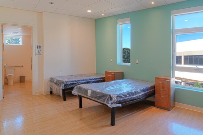 Two single beds with side cabinets against a mint-colored wall. The door to the adjacent bathroom is open