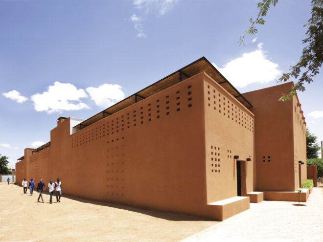 Groups of people walking by long red-brick buildings with thatch terraces