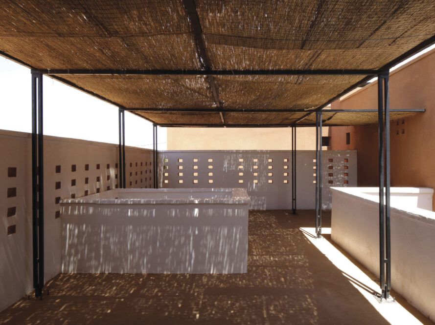 Terrace with tall walls that have rectangular perforations. Terrace is shaded with a thatch canopy