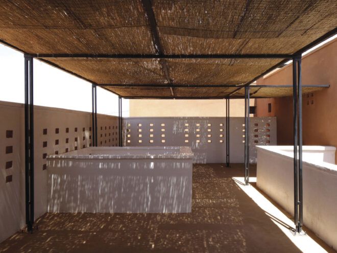 Terrace with tall walls that have rectangular perforations. Terrace is shaded with a thatch canopy