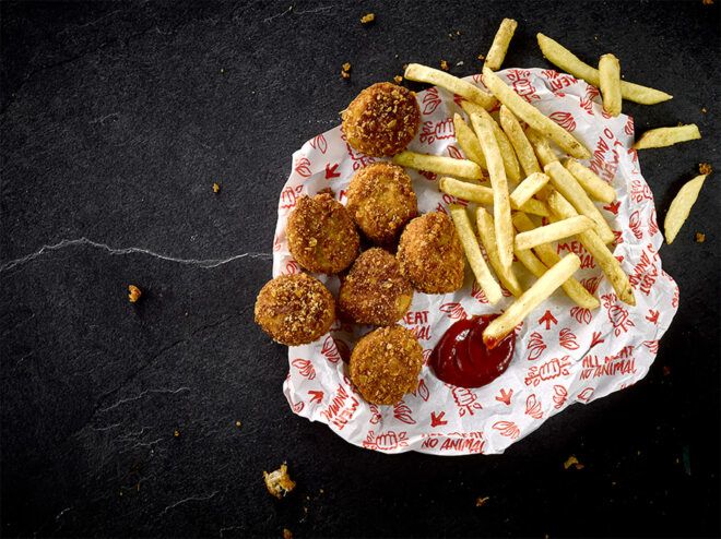 A paper containing vegan chicken nuggets and fries with a dollop of ketchup