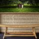 Sleek bamboo bench in front of a large earthy toned frame with intricate patterns and detailing. The frame encompasses a screen that shows two people in a grassy field surrounded by monkeys