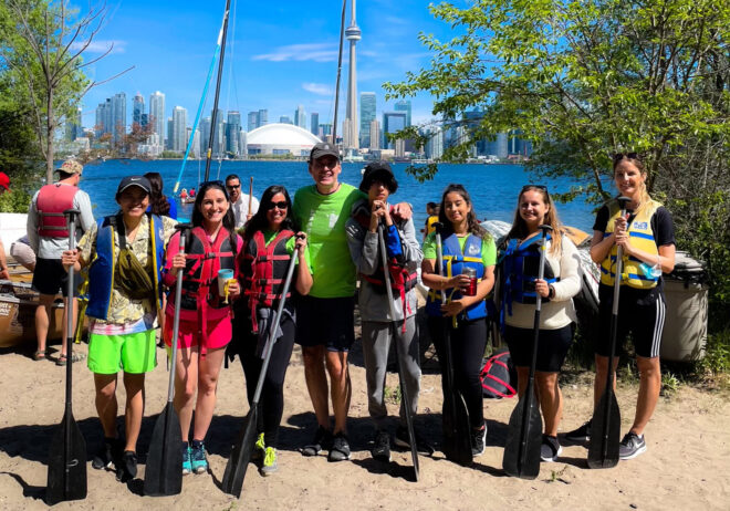 A group of people standing next to each other smiling into the camera with the backdrop of a pier