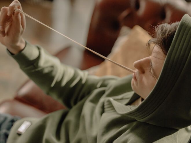 A man wearing a hoodie stretching a gum out of his mouth
