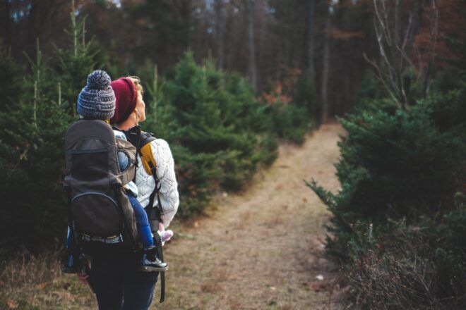 A woman carrying a child on her back hiking through a dirt trail