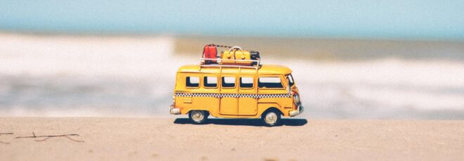 A toy yellow van with luggage on top of it against an ocean background