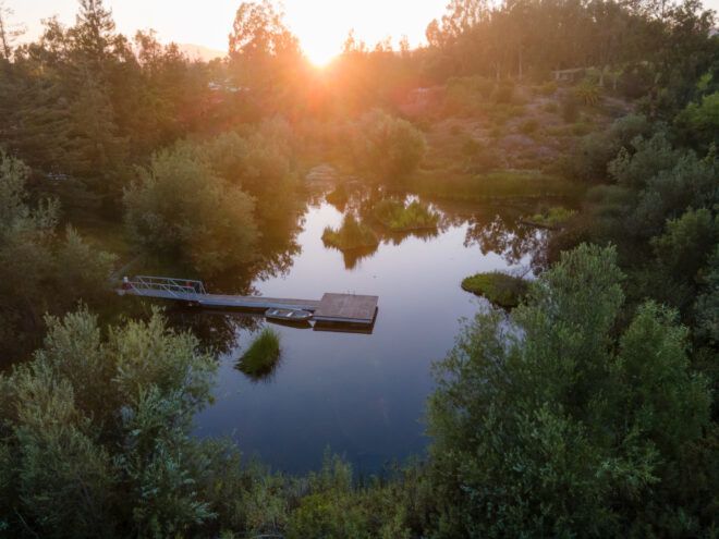 Aerial view of a pond with a dock and small boat at susnset