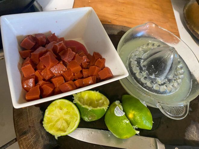 A white square bowl holding faux Current Tuna with used up lime halves in front and a clear lime squeezer with liquid
