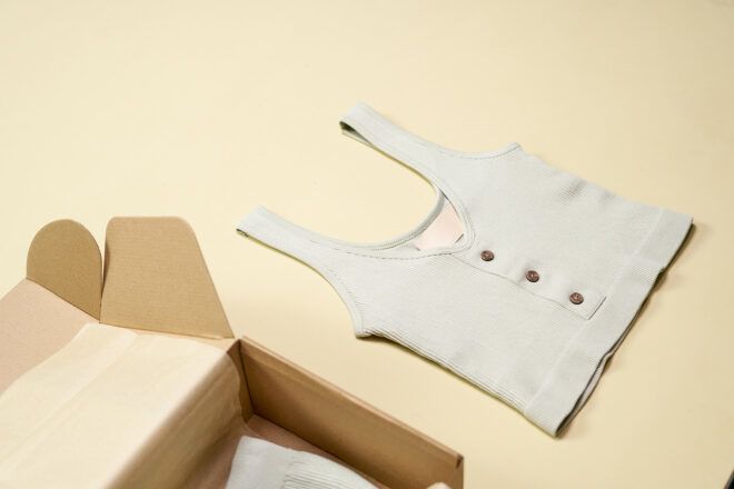 A white tank top laid next to a cardboard box on a cream floor
