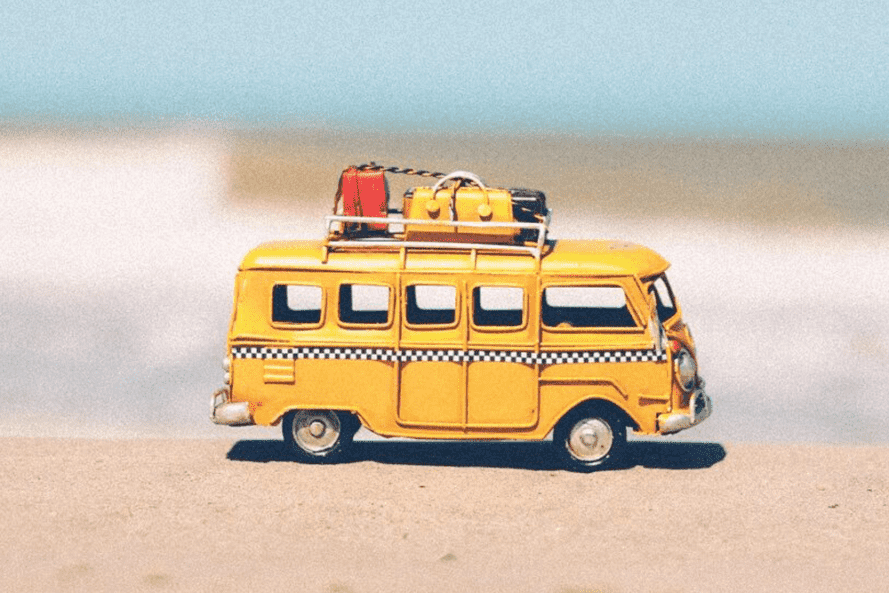 A toy yellow van with luggage on top of it against an ocean background