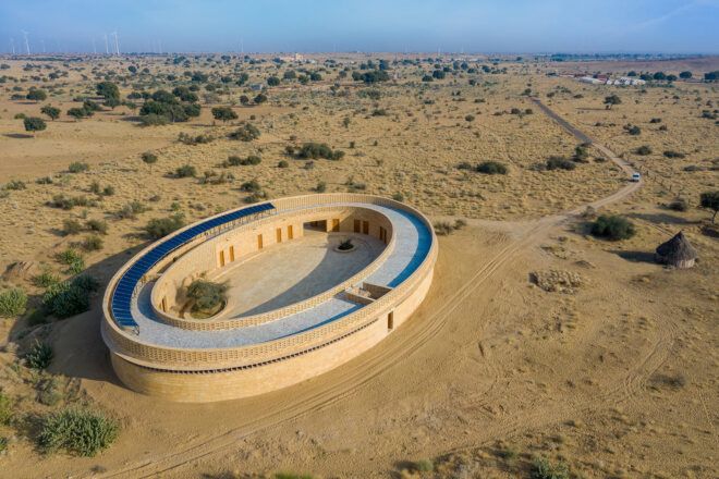 An oval-shaped wooden building in the middle of a desert landscape