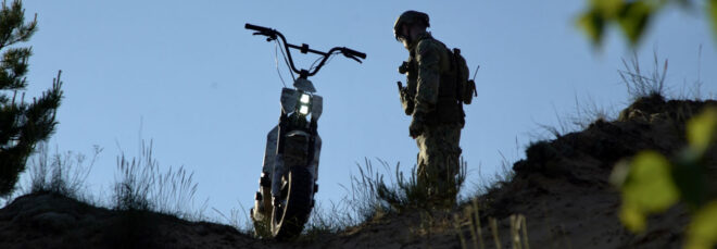 A man in uniform atop a hill and standing next to the scooter