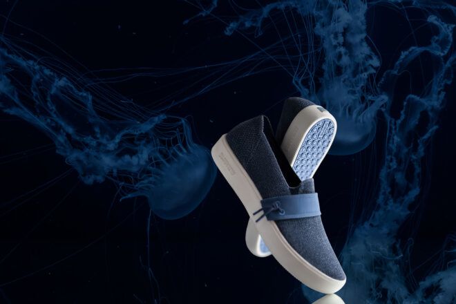 Two blue sneakers displayed to cross each other against a black background with blue wisps
