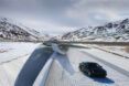 A black car driving on a white pathway surrounded by a mountain landscape