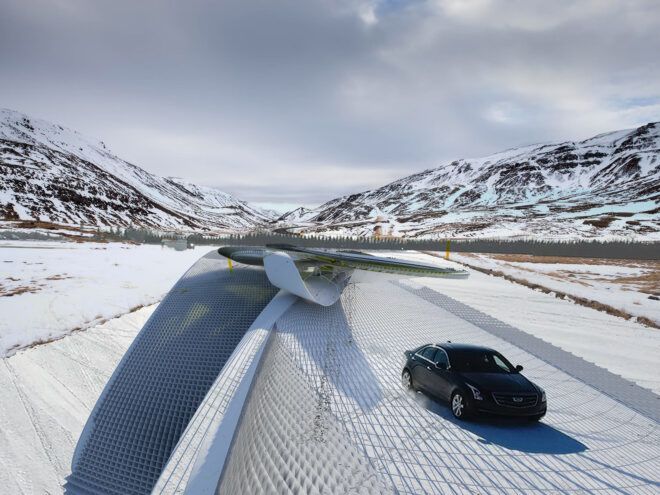 A black car driving on a white pathway surrounded by a mountain landscape