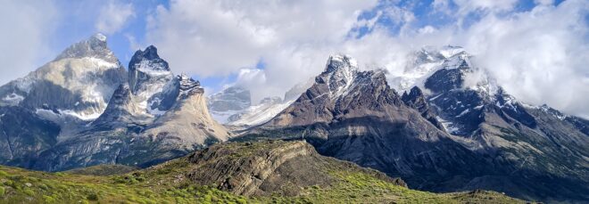 A mountain range in Chile with clouds in the background and green hills in the foreground