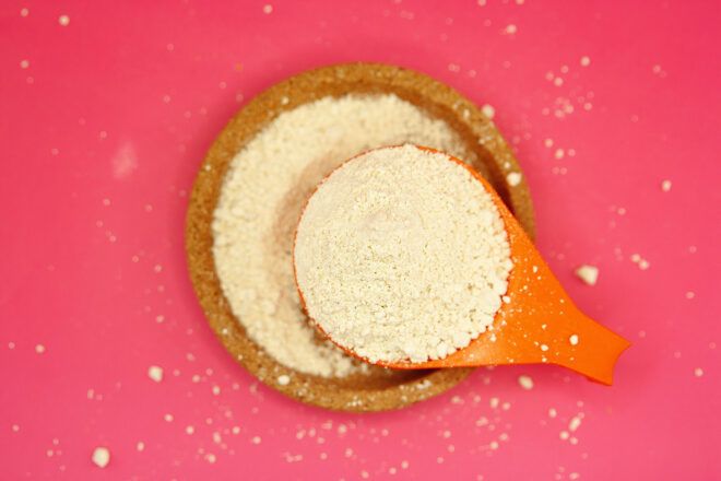 A white grain powder in a wooden bowl lifted by a wooden spoon
