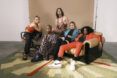 A group of five people wearing fashionable clothes and lounging on or around a sofa