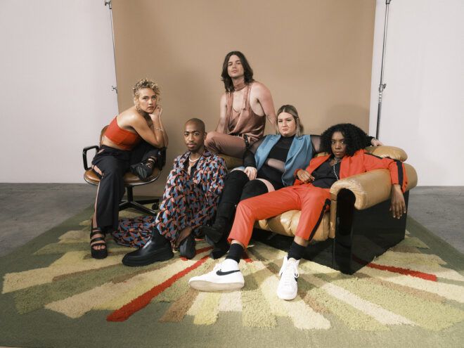 A group of five people wearing fashionable clothes and lounging on or around a sofa