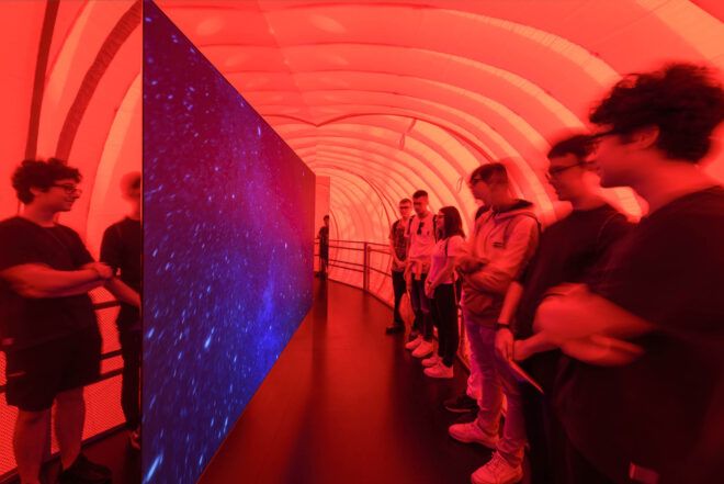 An interior red area with people observing a sheet of blue board