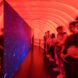 An interior red area with people observing a sheet of blue board