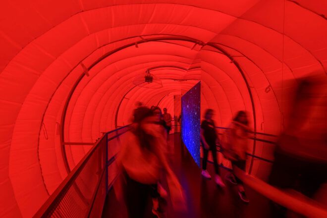 People walking within a red tube passing through a blue divider