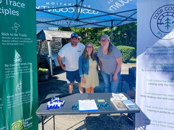 Three people with their arms around each other standing behind a table with two posters on either side of them