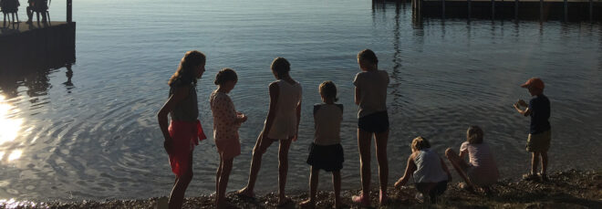 A row of children playing aside the edge of a lake