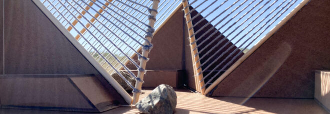 Interior of Vergence Pavilion. Parts of the interior are in shade while the sun casts interlacing grid pattern on the deck below from the jute rope canopy