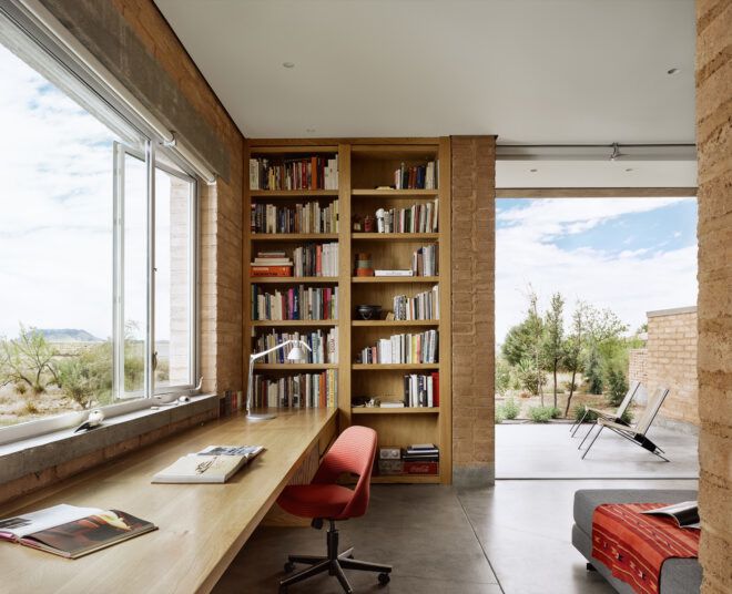 A workspace with an open window and an open doorway with a bookshelf that lines one wall
