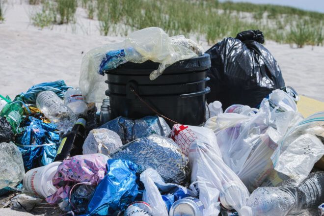 A beach trash can overflowing with plastic bags and bottles